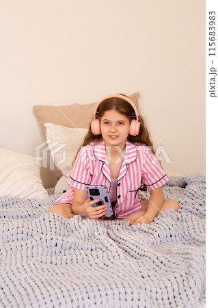 Young girl with headphones using smartphone on bed. Young girl with headphones using smartphone on bed. 115683983