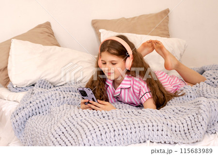 Girl in pink pajamas lying on bed using smartphone. Girl in pink pajamas lying on bed using smartphone. 115683989