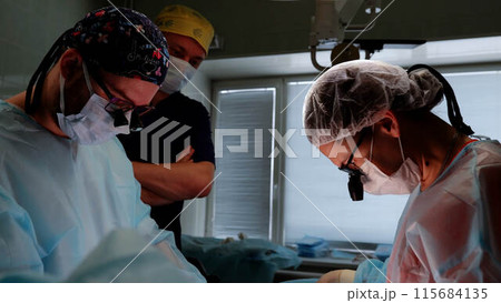 In operating room team of doctors and assistants focuses on performing microsurgery to save patient's life. Modern medicine advanced technologies and expertise of professionals saving lives. In operating room team of doctors and assistants focuses on performing microsurgery to save patient's life. Modern medicine advanced technologies and expertise of professionals saving lives. 115684135