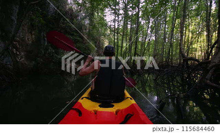 Kayaker in safety gear paddles in river with trees in water 115684460