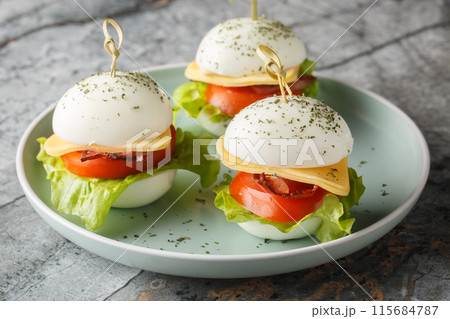 Original breakfast on skewers of hard-boiled eggs with cheese, bacon, tomato and lettuce close-up in a plate. Horizontal 115684787
