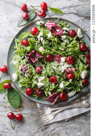Summer salad with berries cherry, arugula, chicory and feta cheese dressed with balsamic sauce close-up in a plate. Vertical top view 115684806