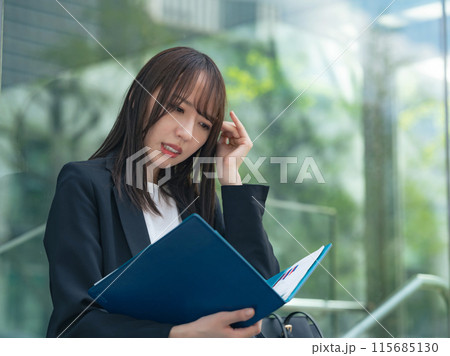 街角で書類を見ながら悩む女性ビジネスウーマン 街角で書類を見ながら悩む女性ビジネスウーマン 115685130