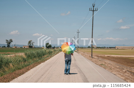 person walking with an open rainbow umbrella 115685424