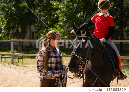 Instructor discusses technique with young rider during equestrian lesson. Instructor discusses technique with young rider during equestrian lesson. 115685839