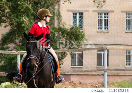 Young rider on horseback looking sideways at stables. Young rider on horseback looking sideways at stables. 115685858