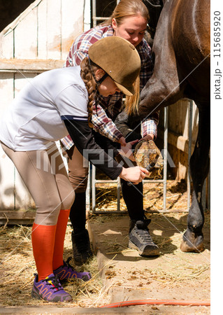 Instructor and young girl clean horse's hoof together. Instructor and young girl clean horse's hoof together. 115685920