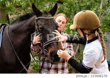 Woman and young rider adjusting bridle on horse. Woman and young rider adjusting bridle on horse. 115686170