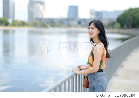 A joyful urban escape by the lake, a young woman in an orange shirt enjoys nature A joyful urban escape by the lake, a young woman in an orange shirt enjoys nature 115686294