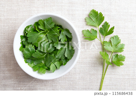 Fresh flat leaf parsley  in a white bowl on linen fabric. Parsley with bright green and not wrinkled leaves. Petroselinum crispum, cultivated as a culinary herb, and used as a garnish and vegetable. 115686438