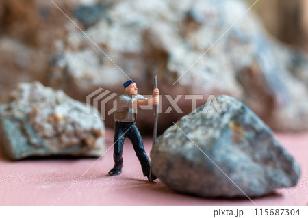 Miniature worker pushing a large rock. Themes of perseverance, strength and labor. This makes it suitable for use in content that involves hard work, challenges, and overcoming obstacles. 115687304