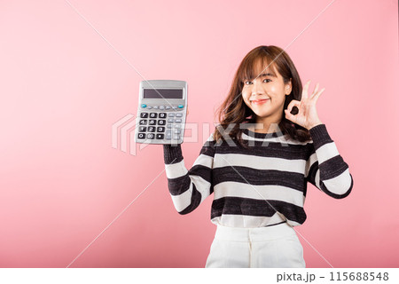 Tax day concept. Woman confident smiling holding electronic calculator and show OK gesture, excited happy Asian female studio shot isolated on pink background, Account and finance counting income 115688548