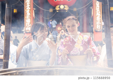 浅草寺で常香炉の煙を浴びる着物姿の外国人女性と案内する日本人女性 115688950