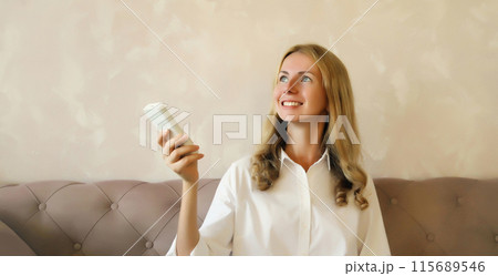 Happy smiling caucasian young woman turns on the air conditioner using the remote control at home Happy smiling caucasian young woman turns on the air conditioner using the remote control at home 115689546