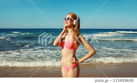 Summer vacation of relaxed happy young woman listening to music with headphones on the beach at sea Summer vacation of relaxed happy young woman listening to music with headphones on the beach at sea 115689600
