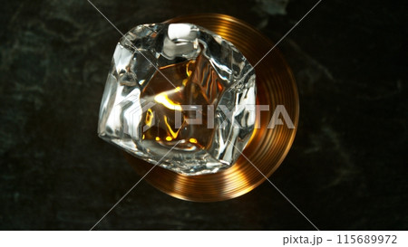 Closeup of ice cube falling into glass of whiskey. 115689972