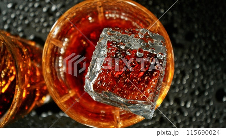 Closeup of ice cube falling into glass of whiskey. Closeup of ice cube falling into glass of whiskey. 115690024
