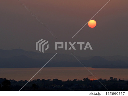 猪苗代湖対岸に沈む夕日。真っ赤な太陽と湖面の赤い輝きが淡い色彩の背景に印象的で綺麗だ。 猪苗代湖対岸に沈む夕日。真っ赤な太陽と湖面の赤い輝きが淡い色彩の背景に印象的で綺麗だ。 115690557
