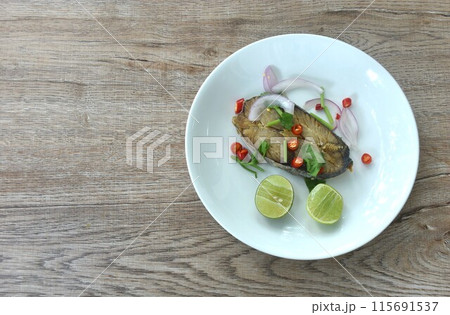 salty dry Indo-Pacific king mackerel fish topping chop shallot and chili with slice lemon salad on plate salty dry Indo-Pacific king mackerel fish topping chop shallot and chili with slice lemon salad on plate 115691537