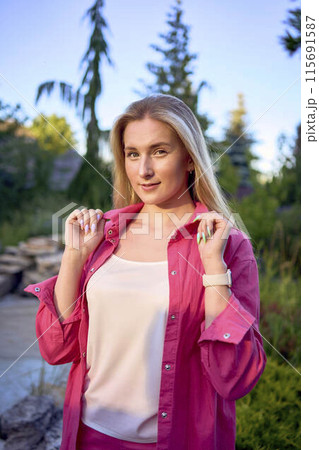 portrait of a young blonde woman in hot pink shorts and shirt near an artificial waterfall 115691587