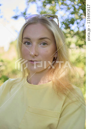 a portrait of a young blond girl in a yellow T-shirt and shorts among the trees on a summer day a portrait of a young blond girl in a yellow T-shirt and shorts among the trees on a summer day 115691617