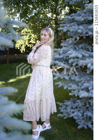 portrait of a young blonde girl in a pastel chiffon dress near a blue Christmas tree 115691635