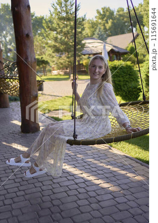 portrait of a young blonde woman in a pastel chiffon dress circling in a wicker hammock portrait of a young blonde woman in a pastel chiffon dress circling in a wicker hammock 115691644