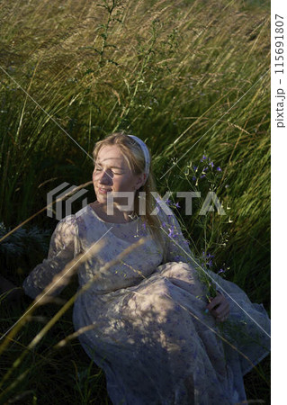 portrait of a young blonde woman in a pastel chiffon dress in a field of golden grass 115691807
