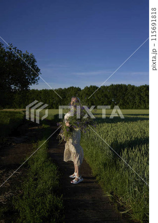 portrait of a young blonde woman in a pastel chiffon dress walking with a giant bouquet of wild flowers in a field 115691818