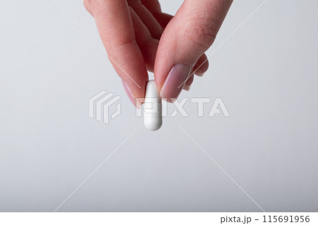 Female hand holding the capsule on white background. Fingers holding pill, closeup. Concept of health care, dietary supplements, vitamins, treatment of depression and diseases. High quality photo Female hand holding the capsule on white background. Fingers holding pill, closeup. Concept of health care, dietary supplements, vitamins, treatment of depression and diseases. High quality photo 115691956