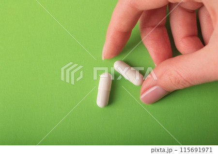 Hand with pills closeup. Medical capsules. Isolated on a green background. An allergy pill, antibiotics, supplements. Medicine, healthcare concept. Virus(viral) and flu diseases. High quality photo Hand with pills closeup. Medical capsules. Isolated on a green background. An allergy pill, antibiotics, supplements. Medicine, healthcare concept. Virus(viral) and flu diseases. High quality photo 115691971