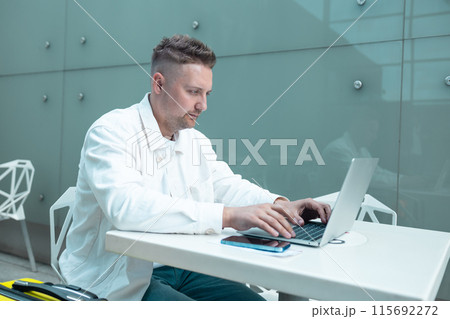 Happy traveling Caucasian man in stylish clothes uses mobile smartphone and laptop, checking trip destination on Internet. Male waiting at flight gates for plane boarding, smiling have a vacation trip 115692272