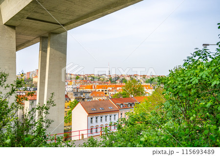 Lush green foliage frames the Nusle Bridge towering over traditional buildings in Prague on a clear spring day. Czechia 115693489