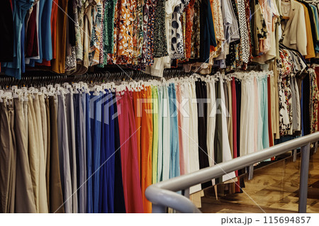Wide variety of colorful clothes on hangers in retail store are arranged by color. Consumerism concept Wide variety of colorful clothes on hangers in retail store are arranged by color. Consumerism concept 115694857