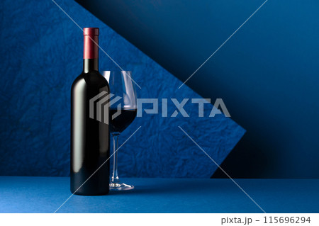 Bottle and glass of red wine on a red background. Bottle and glass of red wine on a red background. 115696294
