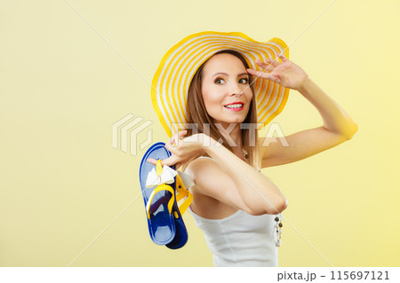 Woman in big yellow summer hat holds flip flops Woman in big yellow summer hat holds flip flops 115697121