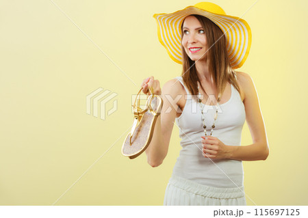 Woman in big yellow summer hat holds sandals Woman in big yellow summer hat holds sandals 115697125