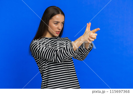 Young woman pointing around with finger gun gesture making choice, shooting killing with hand pistol 115697368