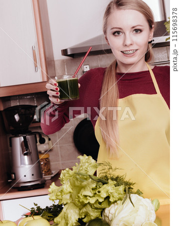 Woman in kitchen holding vegetable smoothie juice 115698378