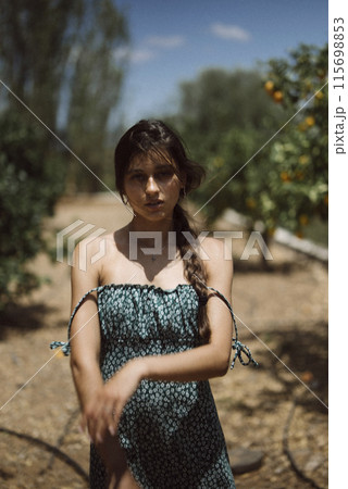 Young woman in summer dress enjoying nature outdoors with greenery and trees in background Young woman in summer dress enjoying nature outdoors with greenery and trees in background 115698853