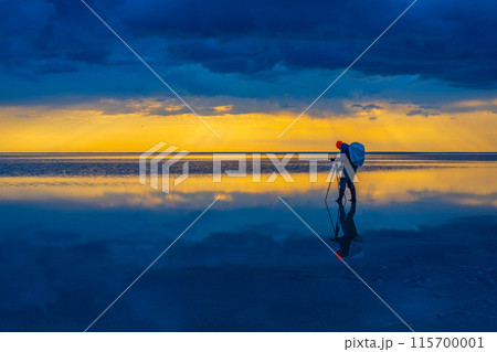 Photographer capturing breathtaking sunset over reflective water scene 115700001