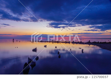 Serene sunset over calm water with dark sky and wooden posts 115700037