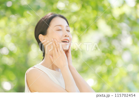 新緑の中で頬を触る女性のビューティー 新緑の中で頬を触る女性のビューティー 115702454