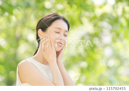 新緑の中で頬を触る女性のビューティー 115702455