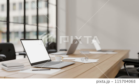 A laptop computer with a white screen mockup on a meeting table in a modern meeting room. 115704068