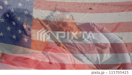 Image of flag of united states of america over senior biracial couple in deckchairs on beach 115705425