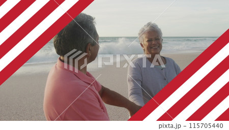 Image of flag of united states of america over senior biracial couple dancing on beach 115705440