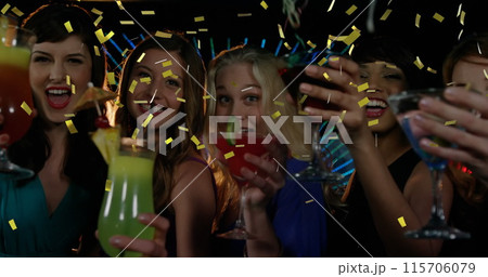Diverse female friends celebrate with drinks in a club as gold confetti falls. 115706079