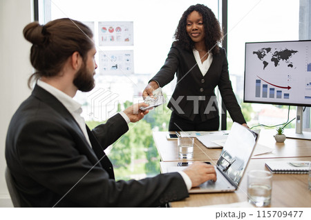 Businesswoman rewarding employee with money in modern office 115709477