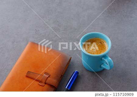 ミルクをたっぷり入れたコーヒーを飲みながら、茶色の革のシステム手帳でデスクワークをしているイメージ ミルクをたっぷり入れたコーヒーを飲みながら、茶色の革のシステム手帳でデスクワークをしているイメージ 115710909